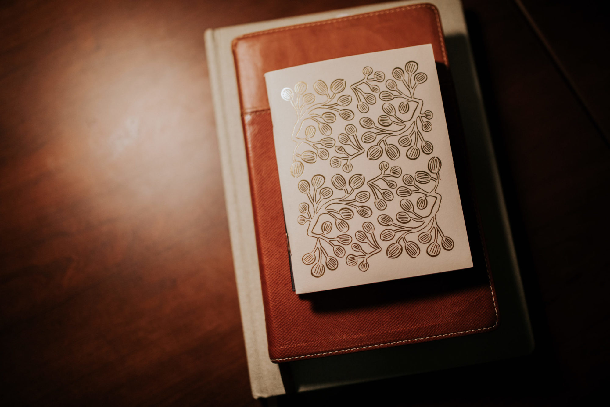 Image of a floral patterned page on top of a leather notebook and a white book.