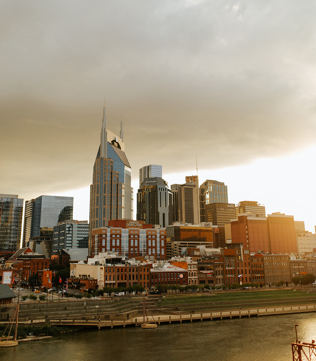 A hazy view of the Nashville city skyline from the Cumberland River, with a large cloud in the background.